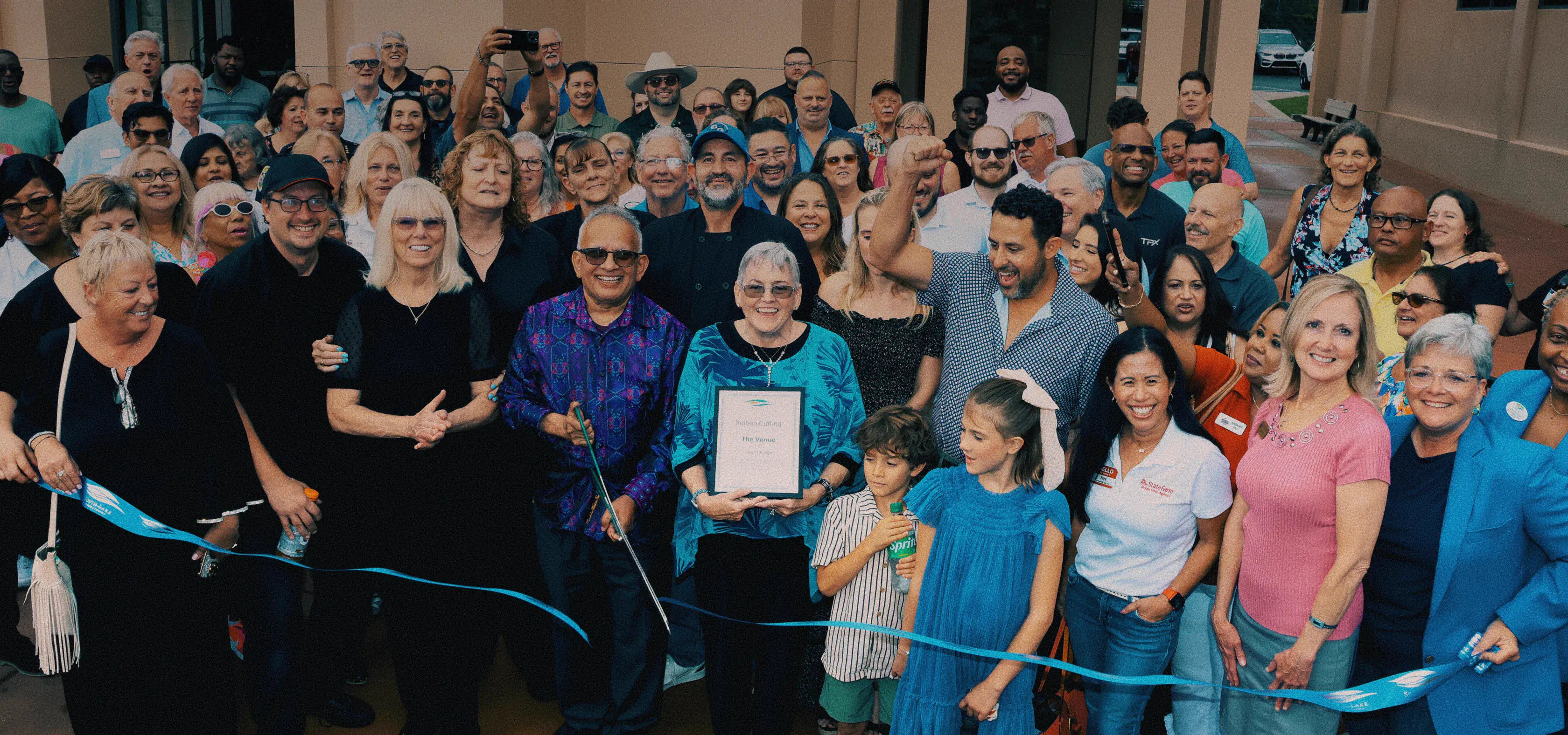 Large crowd of guests and community members at The Venue Clermont ribbon cutting grand opening ceremony with certificate and blue ribbon
